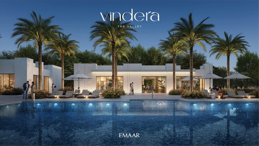 A modern, white villa with large windows, surrounded by palm trees, is reflected in a blue pool at dusk. Several people relax poolside under umbrellas. The words "Vindera The Valley" and "Emaar" are displayed.