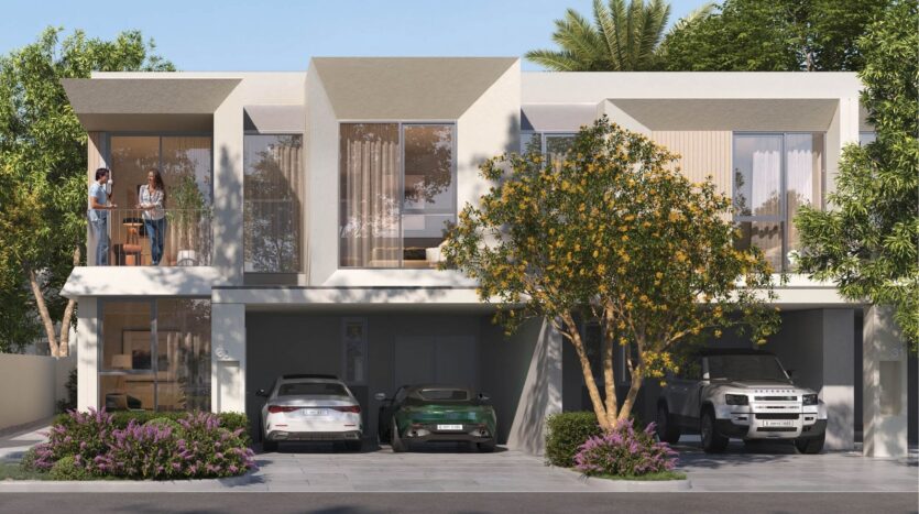 Modern two-storey house with large windows, balconies and garage. Three cars are parked in front of the house and two people stand on a balcony. Green trees and shrubs surround the building.