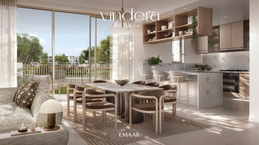 A sunny, modern living and dining room, with marble kitchen, wooden dining table, beige chairs, large windows and a view of lush outdoor space. The words "Vandera, The Valley" and "EMAAR" are displayed on the image.
