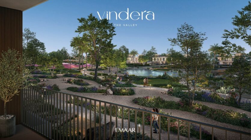 View from a balcony overlooking landscaped gardens, walking paths, trees and a pond with modern villas in the background. The sky is clear and blue. The words "Vindera The Valley EMAAR" are displayed at the top.