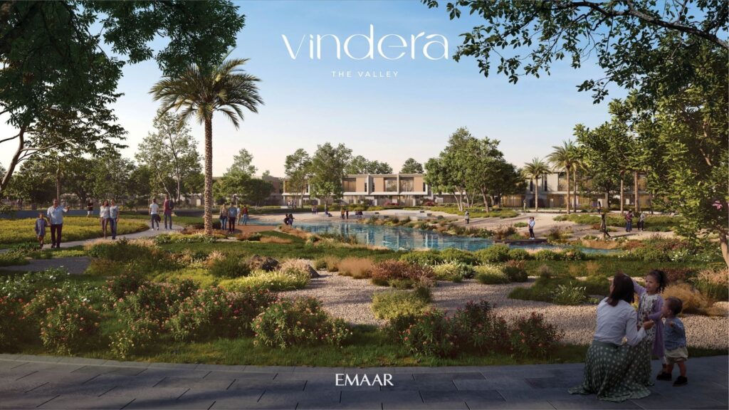 A landscaped park with paths, palm trees and a pond. People stroll and relax; a woman and child are in the foreground. Modern residential buildings can be seen in the background. The "Vendera The Valley" and "Emaar" logos are visible.
