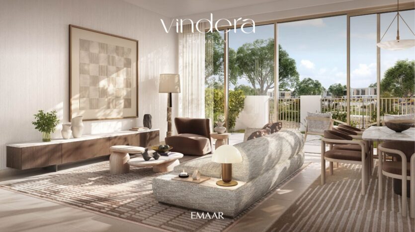 Modern living room with large windows, neutral-toned furniture, gray sofa, coffee tables, patterned carpet and greenery seen through glass doors. The art, decoration and soft lighting create a comfortable, elegant atmosphere.