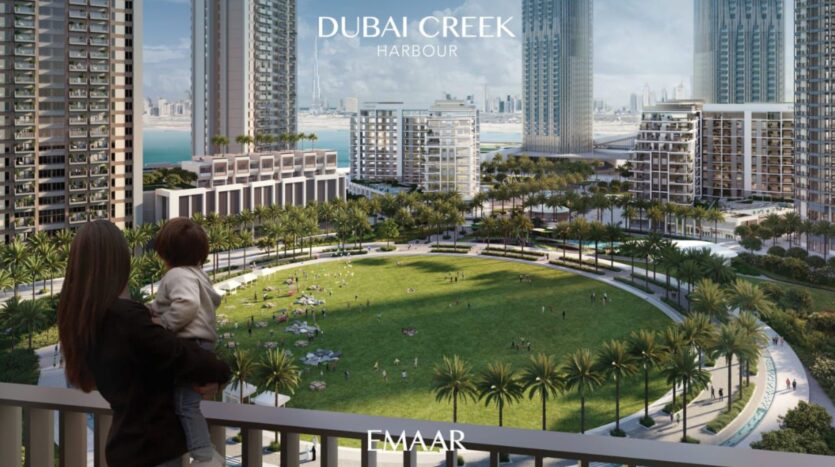 Una donna con in braccio un bambino si trova su un balcone del Lyvia by Palace Residence nel porto di Dubai Creek, affacciato su un parco verde circolare con palme e torri moderne, con sopra la scritta "Dubai Creek Harbour" e "Emaar".