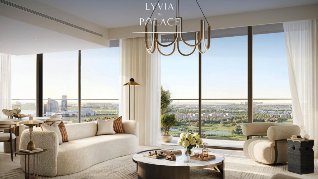 L'elegante e moderna lounge del Lyvia by Palace at Dubai Creek Harbour è caratterizzata da arredi color crema, grandi finestre a tutta altezza con vista sulla città e sui paesaggi lussureggianti, un tavolino rotondo ornato di fiori e un lampadario contemporaneo in alto.