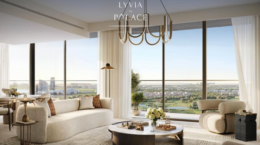 L'elegante e moderna lounge del Lyvia by Palace at Dubai Creek Harbour è caratterizzata da arredi color crema, grandi finestre a tutta altezza con vista sulla città e sui paesaggi lussureggianti, un tavolino rotondo ornato di fiori e un lampadario contemporaneo in alto.