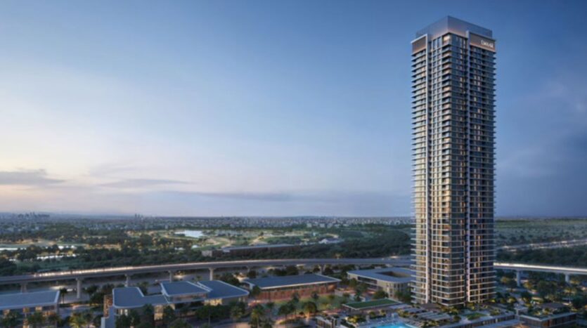 Una grande torre moderna, il Lyvia by Palace Residence nel porto di Dubai Creek, si staglia contro un cielo crepuscolare, circondata da strutture basse, verde e un lontano paesaggio urbano con strade e campi visibili.