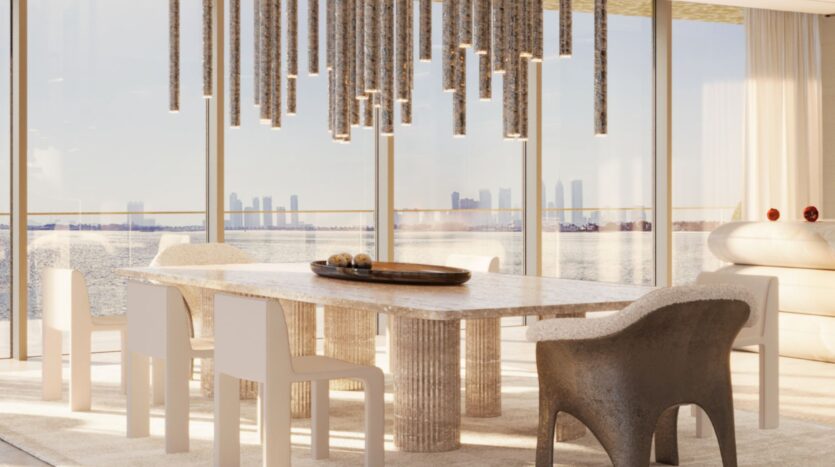 Современная столовая, вдохновленная проектом Maison Margiela Residences, включает каменный стол, стулья в смешанном стиле и скульптурный подвесной светильник. Окна от пола до потолка открывают вид на городской пейзаж и воду, наполняя пространство естественным светом.