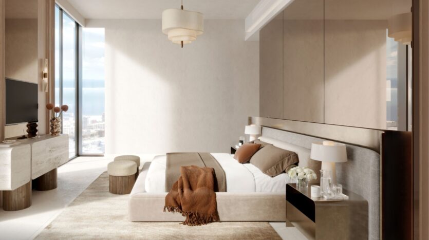 La chambre à coucher moderne aux tons neutres du Portside Square Mina Rashid se compose d'un grand lit avec une couverture brune, de deux tables de chevet avec lampes, d'une télévision sur console, d'une fenêtre allant du sol au plafond et d'une lumière naturelle douce qui remplit l'espace élégant.