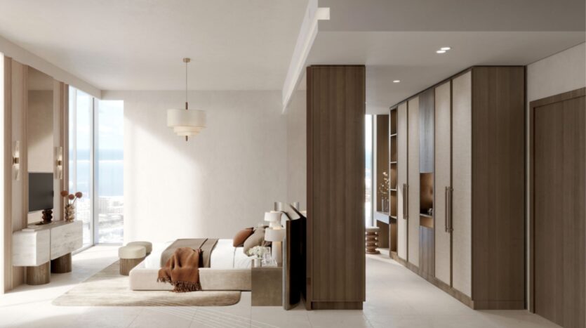 Salon moderne et minimaliste avec des tons neutres, un canapé beige, un jeté marron, une télévision, des armoires en bois encastrées et de grandes fenêtres offrant une vue sur l'océan et les bâtiments de la ville de Portside Square Mina Rashid à l'extérieur.