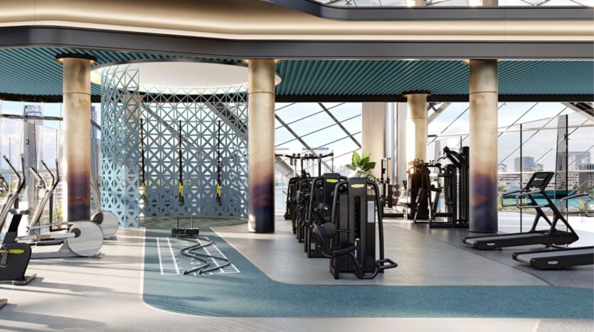 Salle de sport moderne et spacieuse au Portside Square Mina Rashid avec de grandes fenêtres, des machines cardio, des tapis de course, des équipements de résistance et une cloison décorative bleue. Les bâtiments de la ville sont visibles à l'extérieur. La salle est lumineuse et élégante.
