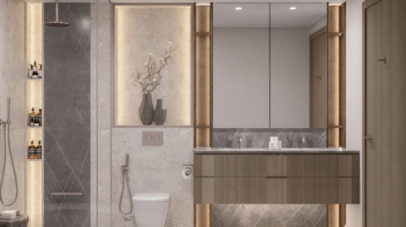 Salle de bains moderne à Portside Square Mina Rashid avec une palette de couleurs grises et beiges, un meuble-lavabo flottant avec sous-éclairage, des étagères éclairées pour les articles de toilette, des toilettes murales et des vases décoratifs avec des branches sur une étagère encastrée.