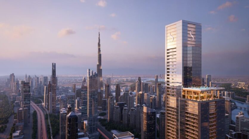 A city skyline at sunset features many modern skyscrapers. The tallest building, the Burj Khalifa, stands among other skyscrapers and SkyParks nestled atop the rooftops. The sky shines with a soft, warm glow and a few clouds drift by.