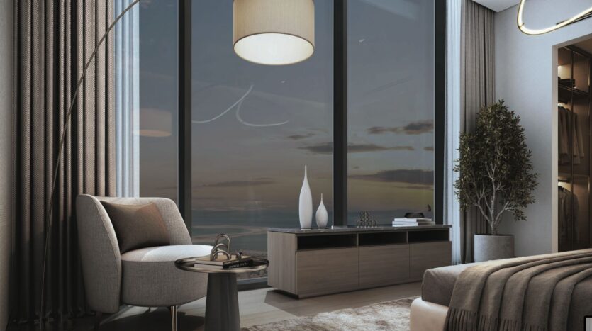 A modern SkyParks bedroom in gray and beige tones includes a comfortable chair, a small side table, a large window with sunset views, a floor lamp, decorative vases and a potted plant next to a bed with a neutral blanket.
