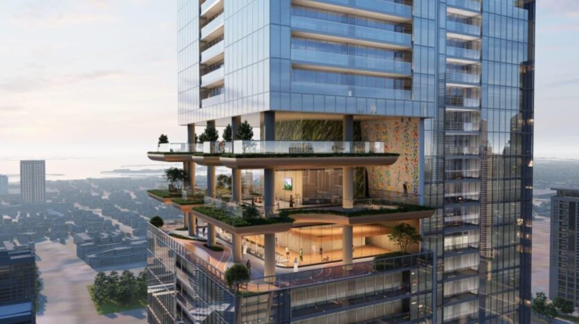 A modern high-rise building featuring an open-air SkyParks terrace with trees, plants and people walking around. The glass-enclosed terrace overlooks a cityscape filled with tall buildings, beautifully illuminated at sunset.