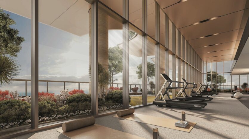 A modern SkyParks gym with large floor-to-ceiling windows, exercise mats, water bottles and treadmills. Flowers and lush greenery are visible outside, offering picturesque views and natural sunlight.