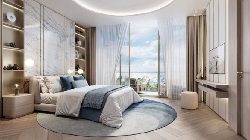 Una moderna camera del Sunset Bay Grand Residence by Imtiaz a Dubai Islands è dotata di letto king-size, biancheria da letto blu e bianca, moquette circolare, finestre a tutta altezza, tende trasparenti, vista sull'oceano e lussuosi tocchi di marmo e legno.