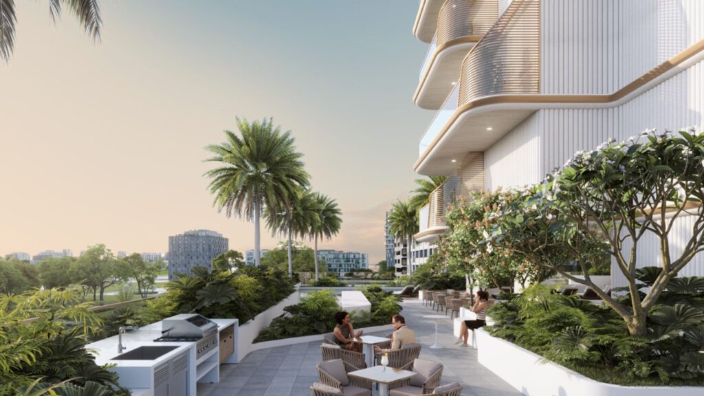 Una moderna terrazza all'aperto presso il Sunset Bay Grand Residence di Imtiaz a Dubai Islands, con persone sedute ai tavoli in mezzo al verde e alle palme accanto a un edificio contemporaneo con balconi curvi; la vista sulla città incornicia il cielo limpido.