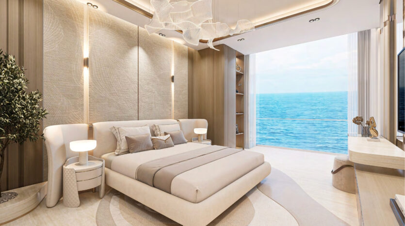 The modern, elegant bedroom in beige and cream tones at Breez by Danube Maritime City features a king-size bed, elegant lighting, floor-to-ceiling windows with ocean views, plus a desk, TV and potted plant for serene luxury.