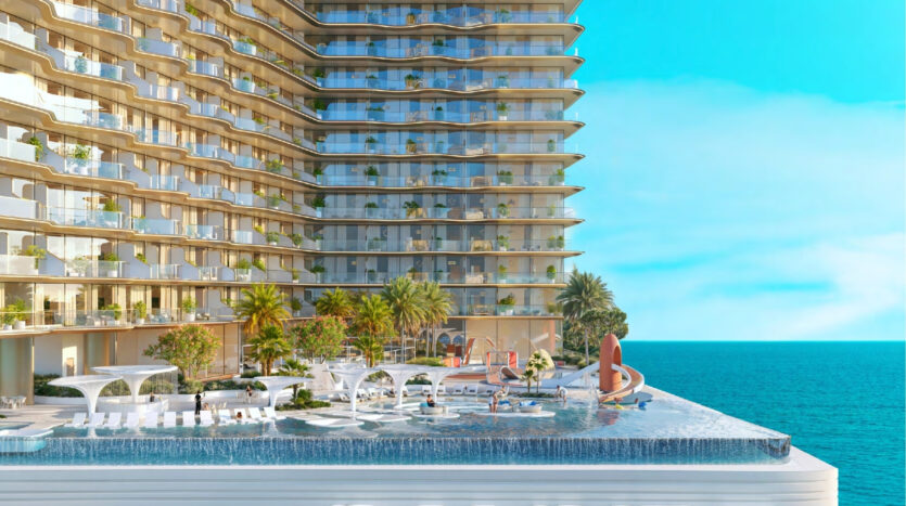 The modern high-rise Breez by Danube Maritime City, with its curved balconies, overlooks an infinity pool, sun loungers, palm trees and landscaped gardens, set against a backdrop of brilliant blue sea and clear sky.