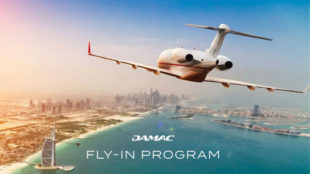 Un jet privado sobrevuela la costa de Dubai, con los rascacielos de la ciudad y el Burj Al Arab debajo. El cielo está despejado y el texto dice "DAMAC Fly-In Program".