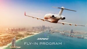 Un jet privato sorvola la costa di Dubai, con i grattacieli della città e il Burj Al Arab in basso. Il cielo è limpido e il testo recita "DAMAC Fly-In Program".