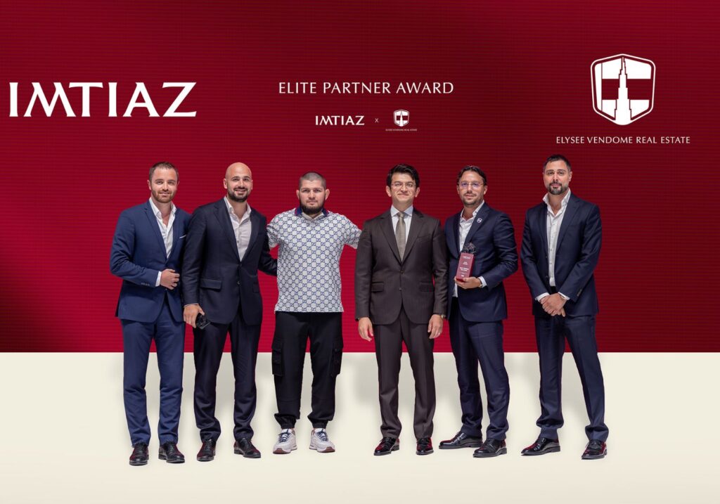 Sechs Männer posieren vor einem roten Hintergrund mit den Logos von Imtiaz, Elysee Vendome Real Estate und den Worten "Elite Partner Award", die die Exzellenz der Immobilienbranche in Dubai hervorheben, während ein Mann stolz eine Trophäe hält.