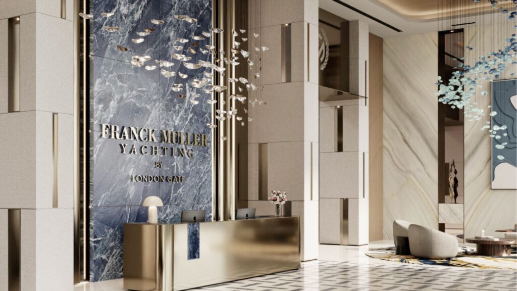Un hall d'entrée moderne et luxueux avec un mur d'accent en marbre affichant "FRANCK MULLER YACHTING 51 LONDON GATE", un bureau de réception métallique, des luminaires sculpturaux et des sièges raffinés - faisant écho à l'élégance de Franck Muller Yachting à Dubaï Maritime City.