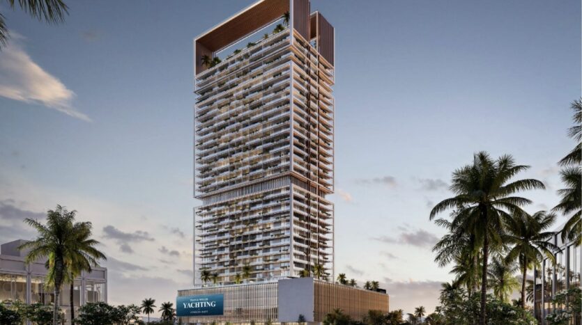 Une tour moderne dotée de nombreux balcons et d'une terrasse sur le toit se dresse au milieu des palmiers au coucher du soleil dans la ville maritime de Dubaï. La partie inférieure comporte un panneau "YACHTING", évoquant l'élégance de Franck Muller Yachting à Dubai Maritime City. Le ciel est partiellement nuageux.