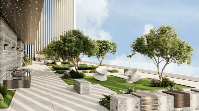 Une terrasse extérieure moderne avec des arbres, des pelouses, des bancs en pierre et des chaises blanches sculpturales, bordée par un grand bâtiment avec un surplomb à motifs et une balustrade en verre, évoque l'élégance de Franck Muller Yachting à Dubai Maritime City.