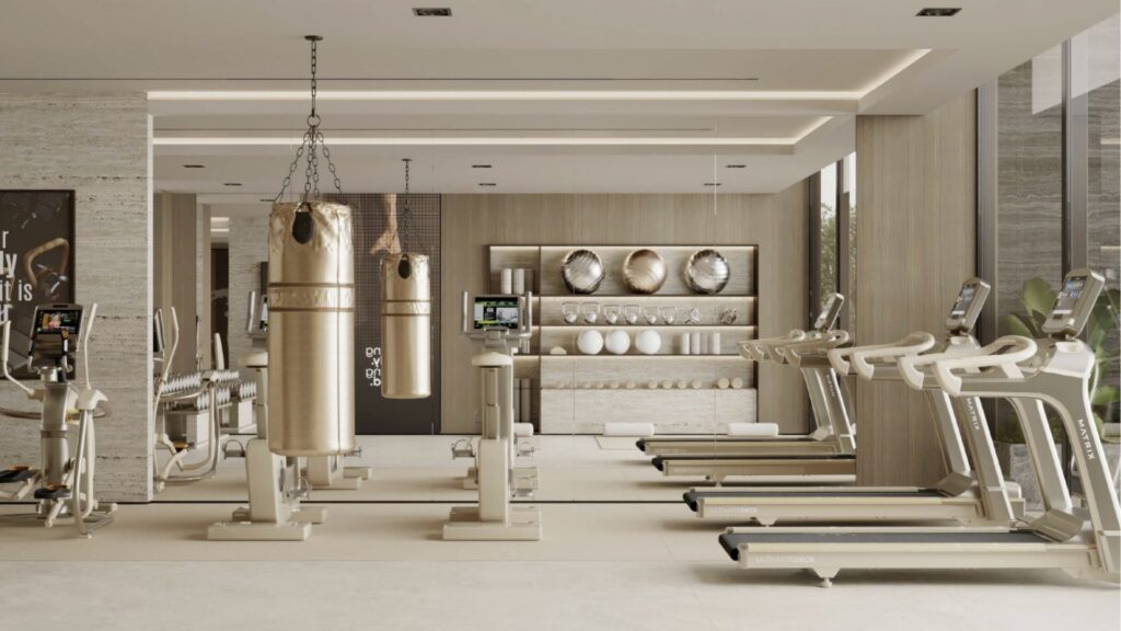 Salle de sport moderne aux tons beiges, équipée de tapis de course, de vélos d'appartement, de sacs de frappe, d'étagères à poids et d'appareils fixés au mur. Inspiré par le Franck Muller Yachting à Dubai Maritime City, l'espace est bien éclairé par de grandes fenêtres et un décor minimaliste.