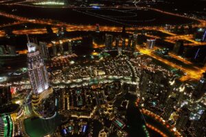 Nächtliche Luftaufnahme einer hell erleuchteten Stadtlandschaft mit hohen Wolkenkratzern, kurvigen Straßen und beleuchteten Gebäuden - perfekt für diejenigen, die in Dubai eine luxuriöse Villa oder ein modernes Apartment inmitten von hellen Straßenlaternen und dunklen offenen Räumen suchen.
