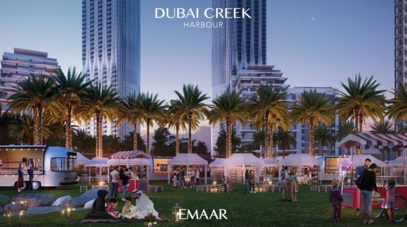 Un vivace mercato all'aperto al tramonto nel porto di Dubai Creek, vicino al Lyvia by Palace Residence, con persone che si godono il cibo, palme, food truck, tende bianche e alti edifici moderni sullo sfondo. Il logo EMAAR è visualizzato in basso.