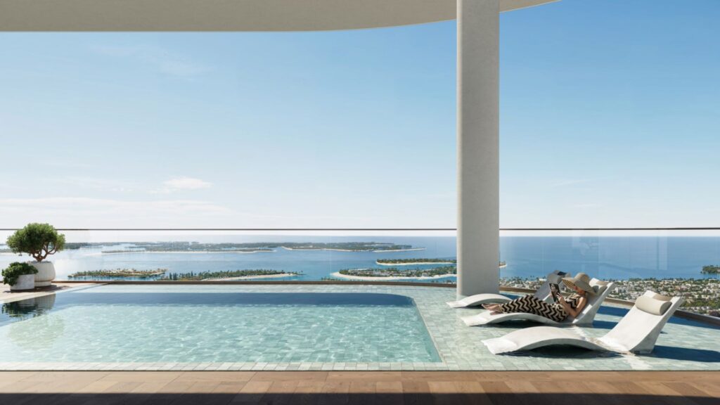 Avarra's modern rooftop infinity pool features loungers overlooking a picturesque coastal landscape with blue waters, small islands and clear skies. Two people relax on poolside loungers under a shaded structure.