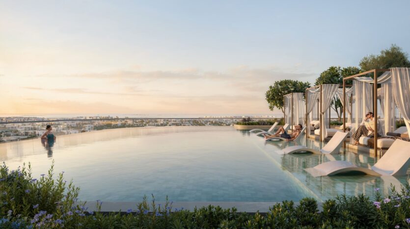 The Avarra's modern rooftop infinity pool is equipped with sun loungers and cabanas at sunset. Guests relax by the water, with the cityscape in the background, surrounded by lush vegetation and vibrant flowers.