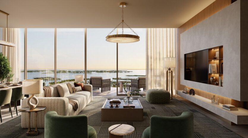 A modern living room with large windows overlooking the waterfront, featuring a beige sofa, Avarra armchairs, coffee table, wall-mounted TV and elegant decor with natural light streaming in.
