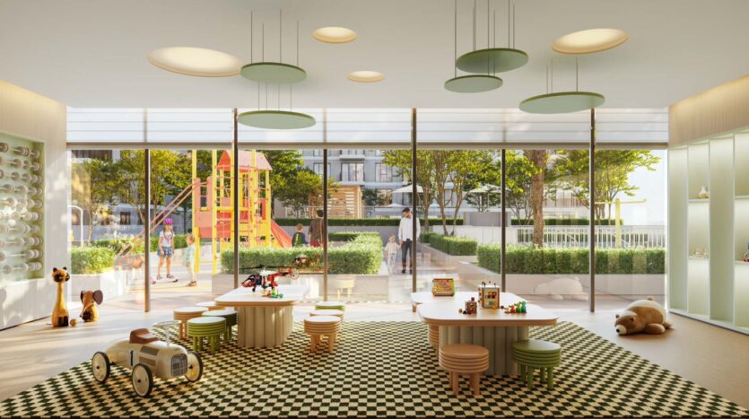 Luminosa sala giochi per bambini con pavimento piastrellato, tavoli in legno e giocattoli. Le grandi finestre si affacciano sull'area giochi Golf Hills con scivolo e bambini che giocano, il tutto circondato dal verde e da edifici moderni.