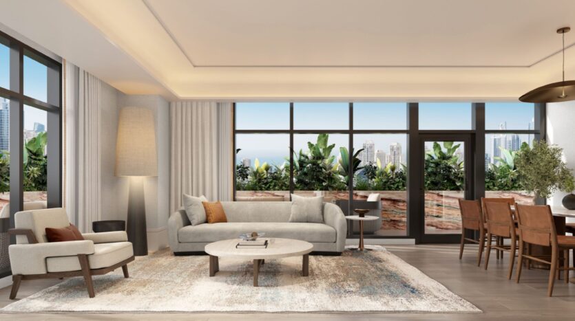 A modern living and dining room in Hilton Residences with large windows, neutral-toned furniture, a round coffee table, a tall lamp and views of city buildings and greenery from the balcony.