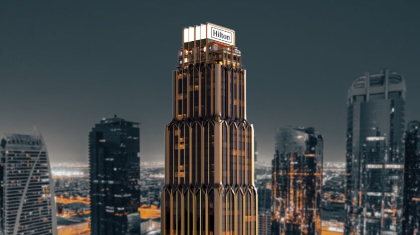 A large modern skyscraper topped by the "Hilton" sign, Hilton residences stand out against a skyscraper cityscape at dusk, with striking gold and dark accents.