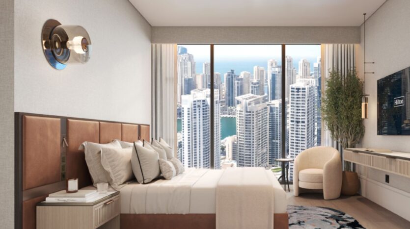 A modern room at Hilton Residences, featuring a king-size bed, wall-mounted TV, desk and upholstered chair, with floor-to-ceiling windows and a breathtaking view of the city skyline with its tall buildings.