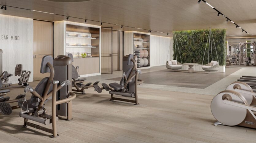Modern, spacious Hilton Residences gym, with exercise equipment, parquet flooring, shelving with towels, a seating area with chairs and plants, and a living green wall in the background. The lighting is warm and the decor minimalist.