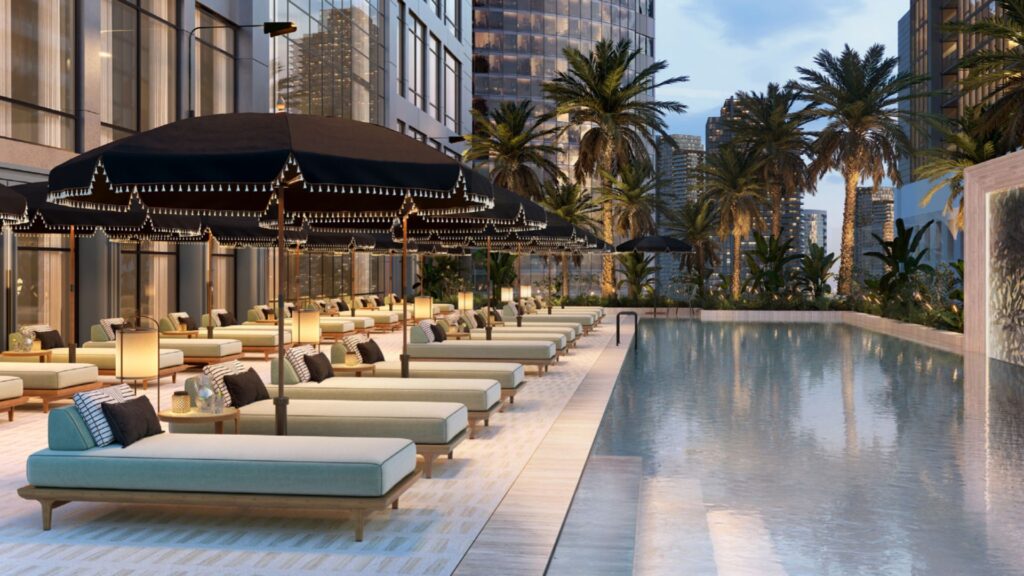 Elegant Hilton Residences outdoor pool with cushioned lounge chairs, black umbrellas, palm trees and the city skyline in the background at dusk. Warm lighting creates a relaxing, luxurious atmosphere.