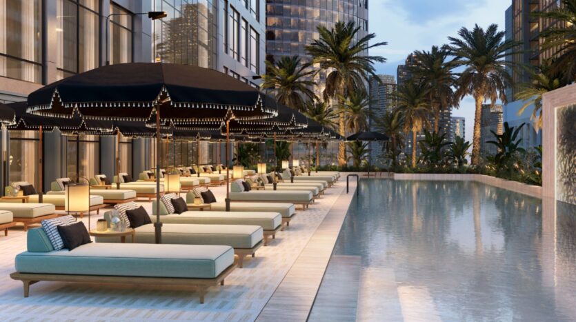 Elegant Hilton Residences outdoor pool with cushioned lounge chairs, black umbrellas, palm trees and the city skyline in the background at dusk. Warm lighting creates a relaxing, luxurious atmosphere.