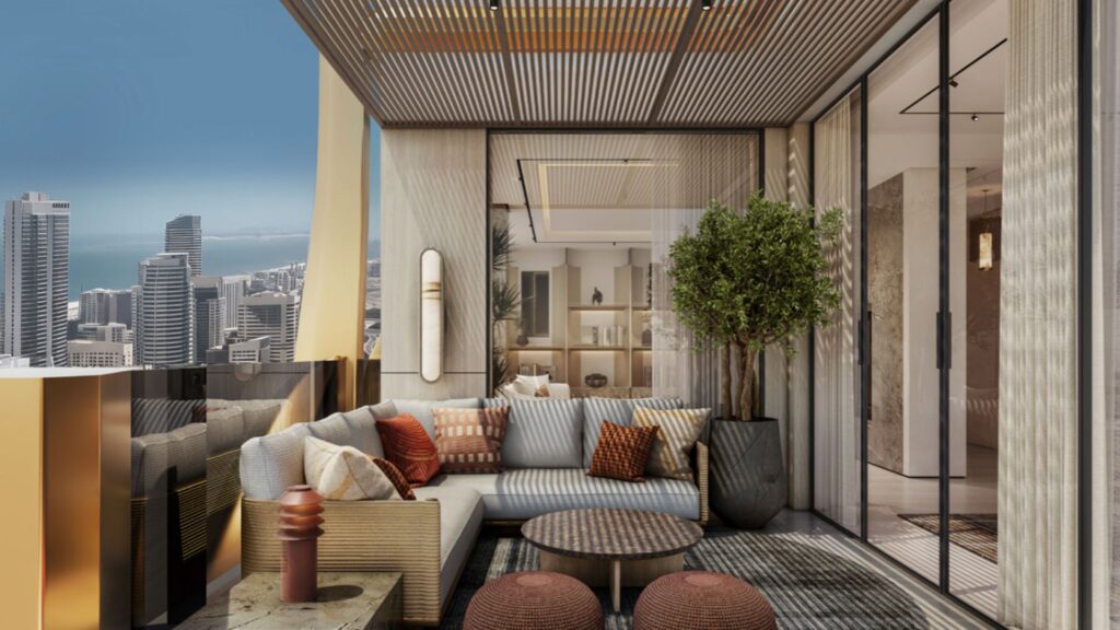 A modern balcony in Hilton Residences with a comfortable seating area featuring a sectional sofa, cushions, round tables, potted plants and a view of the city skyline with tall buildings and water in the background. Glass doors lead to the interior.