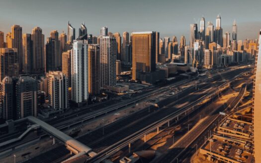 Un paysage urbain comprenant de nombreux immeubles et gratte-ciel, dont les élégantes résidences Hilton, avec une autoroute à plusieurs voies qui traverse le centre, baigné par la lumière chaude du soleil sous un ciel dégagé.