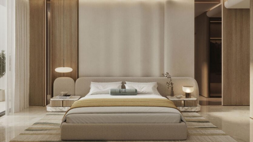 Rabdan Gardens' modern, minimalist bedroom features a low beige bed, white and light brown bedding, two nightstands with round lamps, soft lighting and neutral-toned walls. Vertical wood panels and a striped rug add texture.