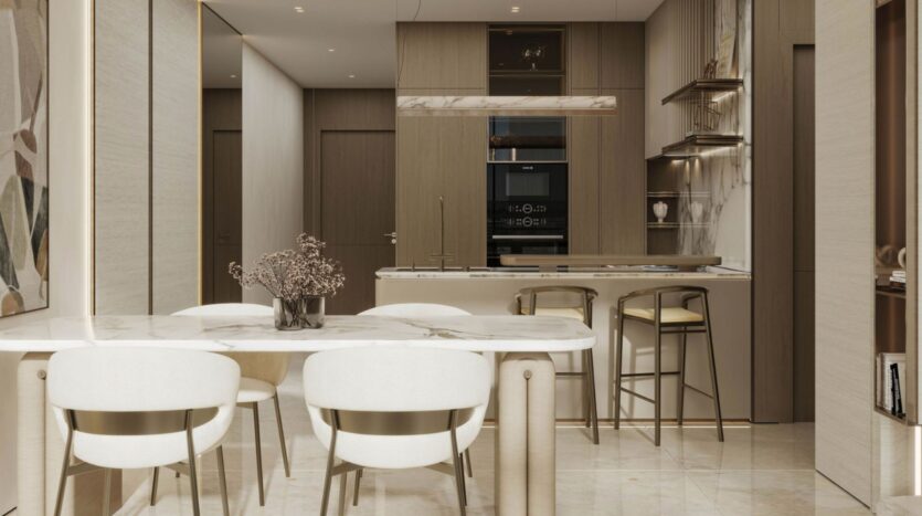 A modern kitchen and dining room in Rabdan Gardens, with a marble table, four white chairs with gold legs, a minimalist island with two bar stools, and neutral-toned cabinetry. A vase with dried flowers adds a warm touch to the space.