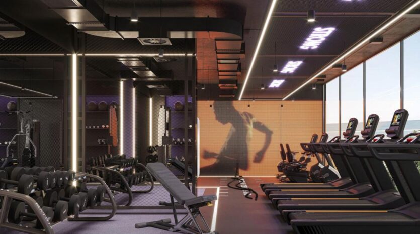 Modern gym in Rabdan Gardens, equipped with treadmills, weight benches, dumbbells, neon lighting and a large wall screen showing the silhouette of a person running. Floor-to-ceiling windows let in natural light.