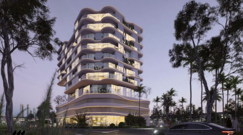 A modern multi-storey building with curved balconies and bright interior lights stands amid palm trees at dusk in the Rabdan gardens, with a car parked nearby and a mauve sky in the background.