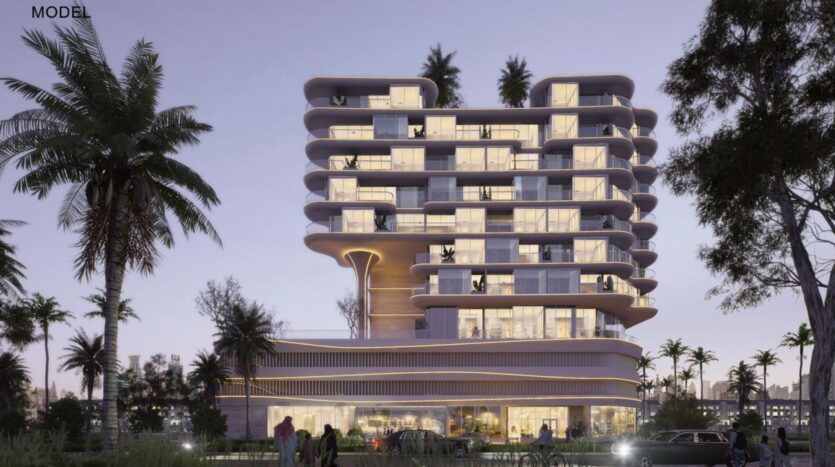 A modern, multi-storey building with rounded edges and large windows is lit up at dusk in the Rabdan gardens, surrounded by palm trees and people walking near the entrance. Cars are parked in front, under a soft purple sky.