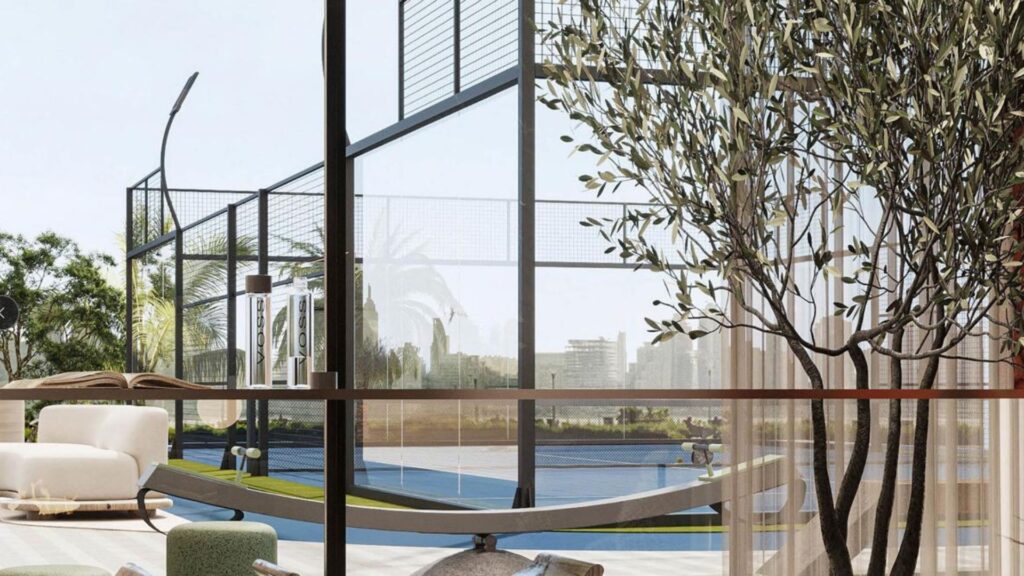 A bright, modern lounge with a white chair, hammock and potted tree inside. The large picture windows of Rabdan Gardens overlook an outdoor padel or tennis court and lush vegetation.